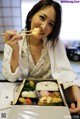 A woman sitting at a table eating a meal with chopsticks.