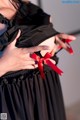 A woman wearing a black dress with a red ribbon tied around her waist.