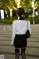 A woman in a white shirt and black skirt is walking down the street.