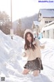 A woman in a white sweater and black skirt playing in the snow.