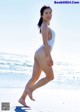 A woman in a white bathing suit walking on the beach.