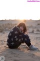 A woman sitting in the sand with a blanket over her head.