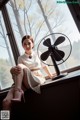 A woman sitting on a window sill next to a fan.